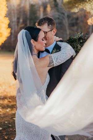 A romantic wedding couple embraces during golden hour as the bride's veil flows dramatically in the autumn breeze.