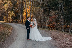 A couple in wedding attire walks along a winding autumn path surrounded by golden fall foliage in the forest.