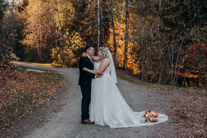 A couple shares an intimate moment on a winding path surrounded by vibrant autumn foliage during their wedding day.