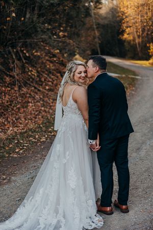 A romantic wedding couple walks hand in hand along a scenic autumn path lined with golden leaves and trees.