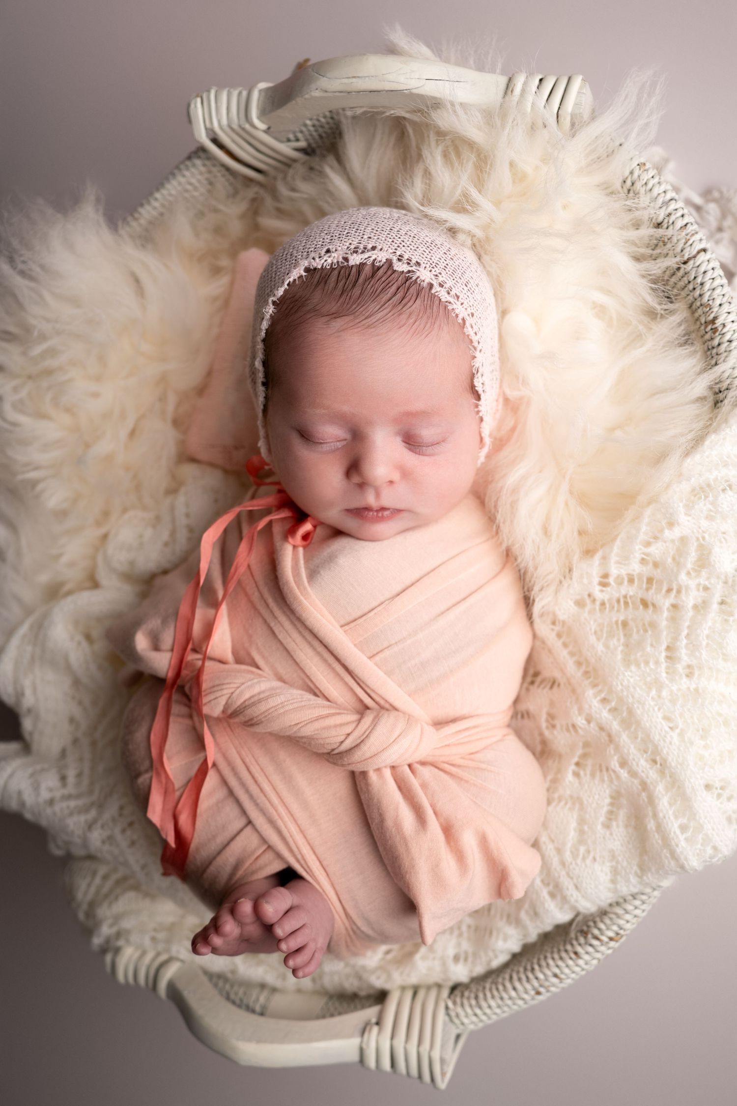 A sleeping newborn swaddled in a soft teal wrap lying on a plush white fur blanket in a professional photo series.
