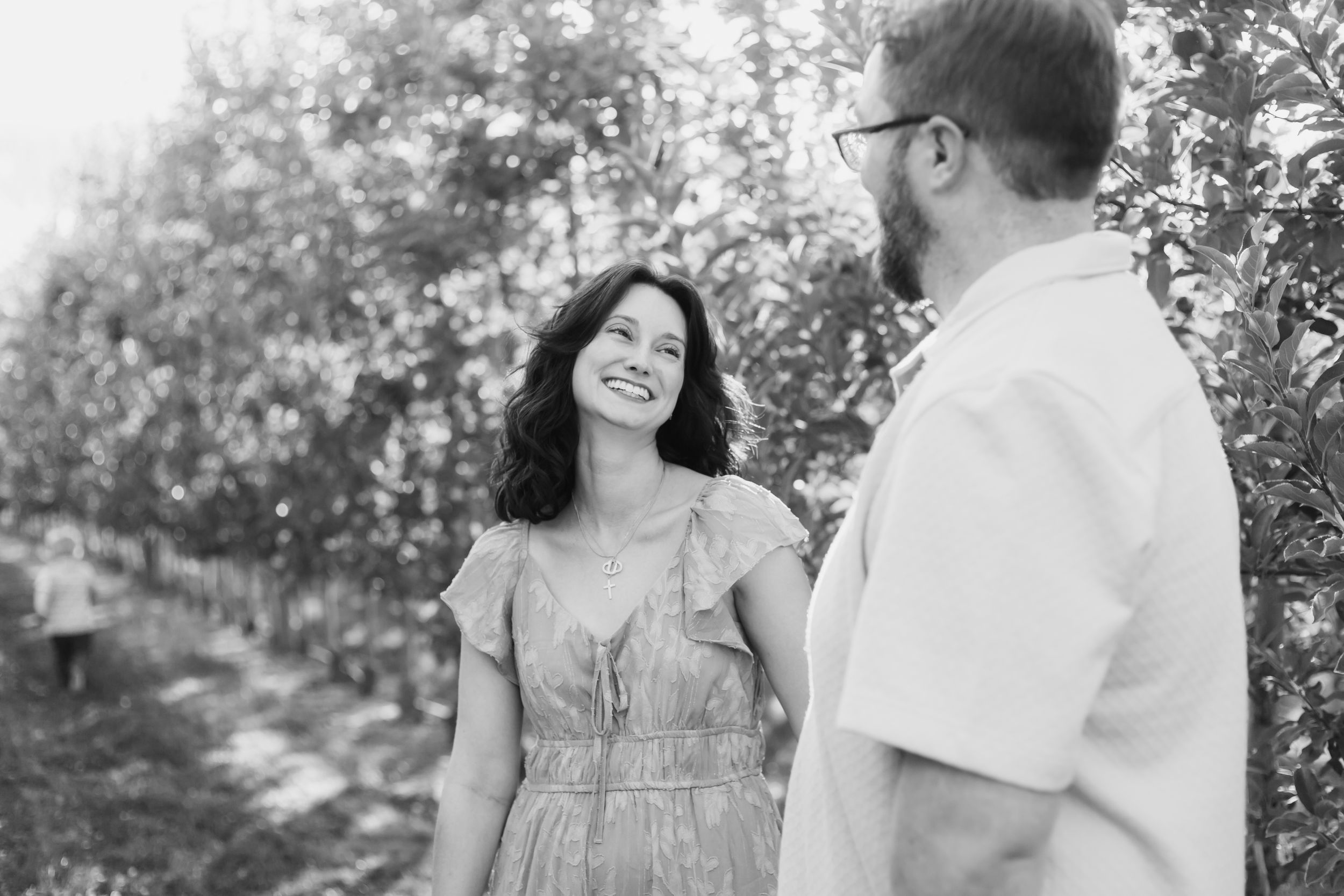 A couple shares a tender moment together outdoors in a black and white photo among trees.