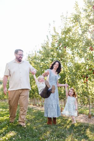 A family enjoys a playful moment together in a sunny orchard during golden hour.