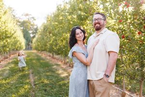 A couple shares a romantic moment together in a scenic apple orchard during sunset.