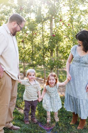 Family enjoying a playful moment together in an apple orchard on a sunny afternoon.