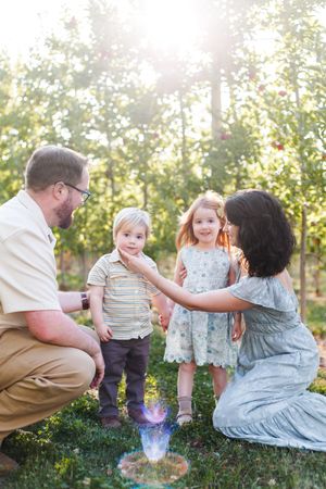 A family enjoys a playful moment together in an orchard on a sunny day.