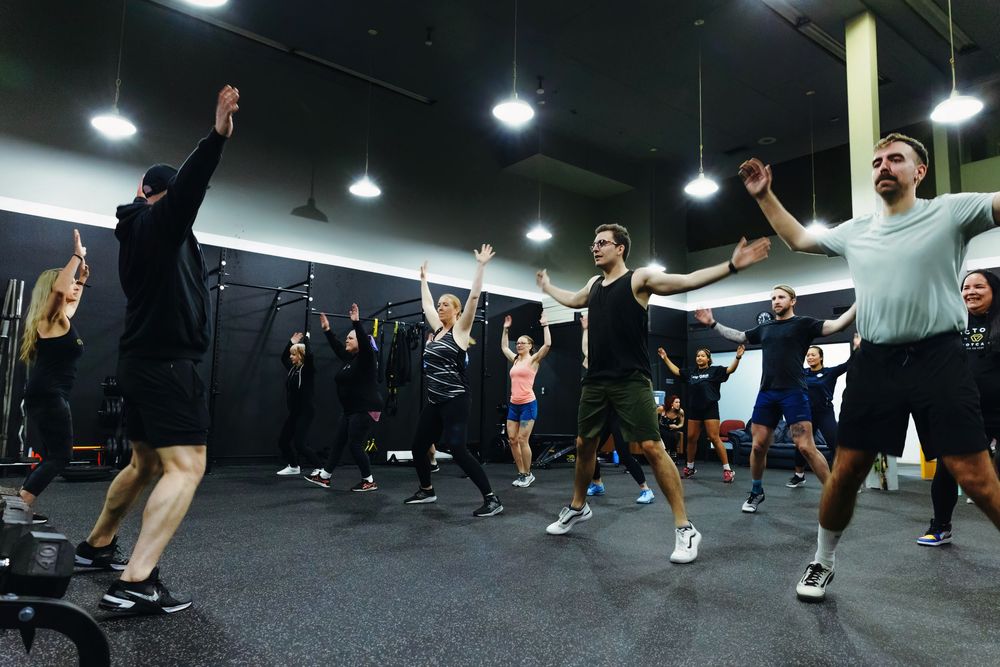 Group fitness class participants exercising together in a dark gym space.