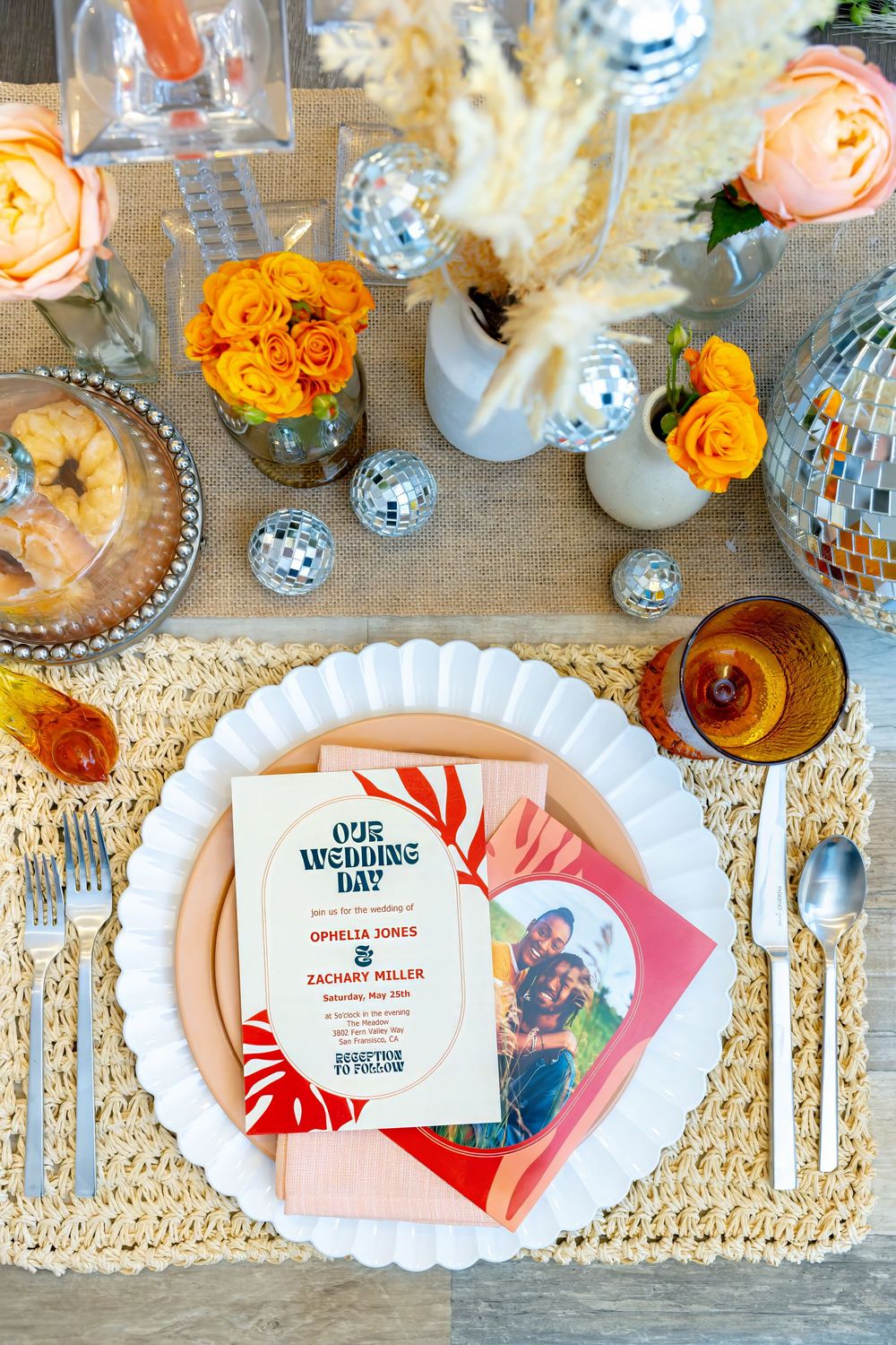 Elegant table setting with orange flowers, glassware and wedding stationery on a lace tablecloth.