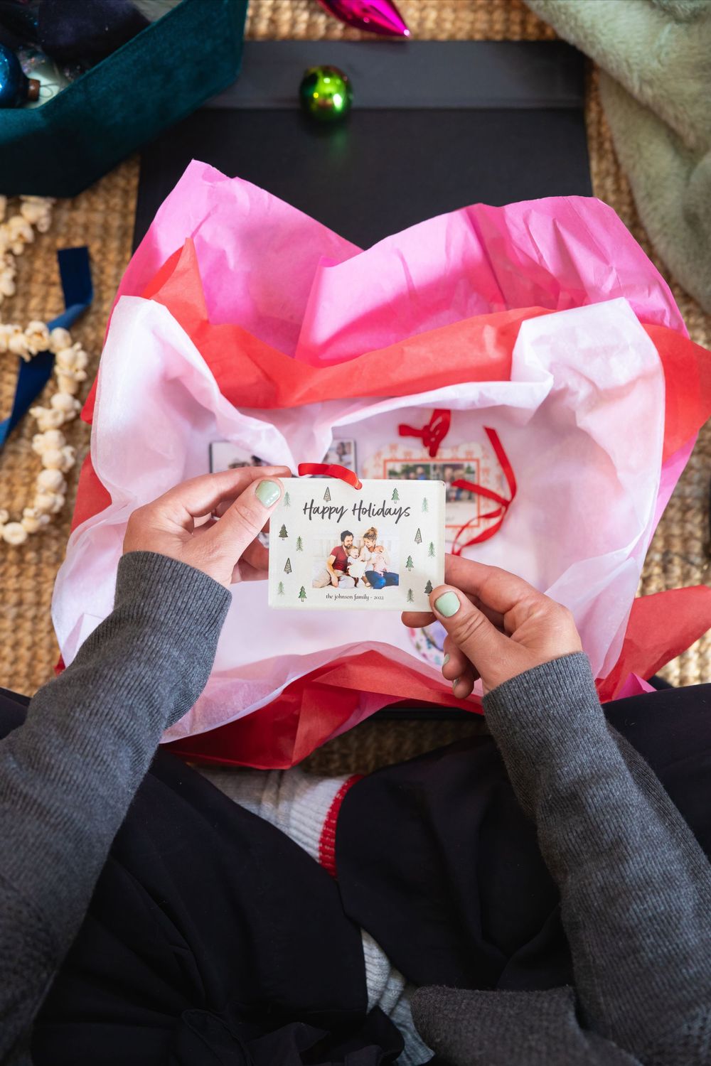 Hands opening a pink gift package containing holiday cards.