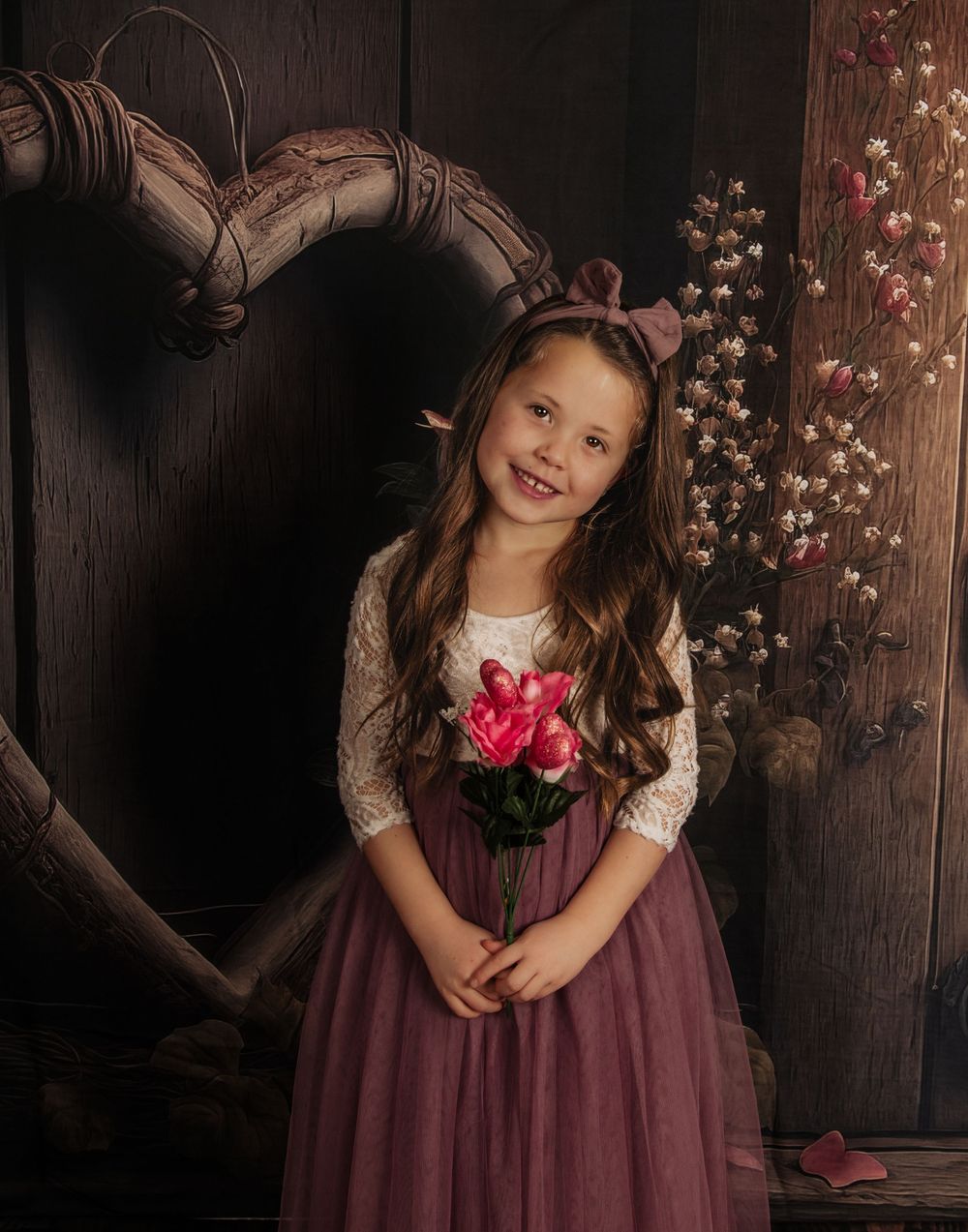 Sweet portrait against wooden wall with heart decor showing someone holding pink roses in a mauve dress.