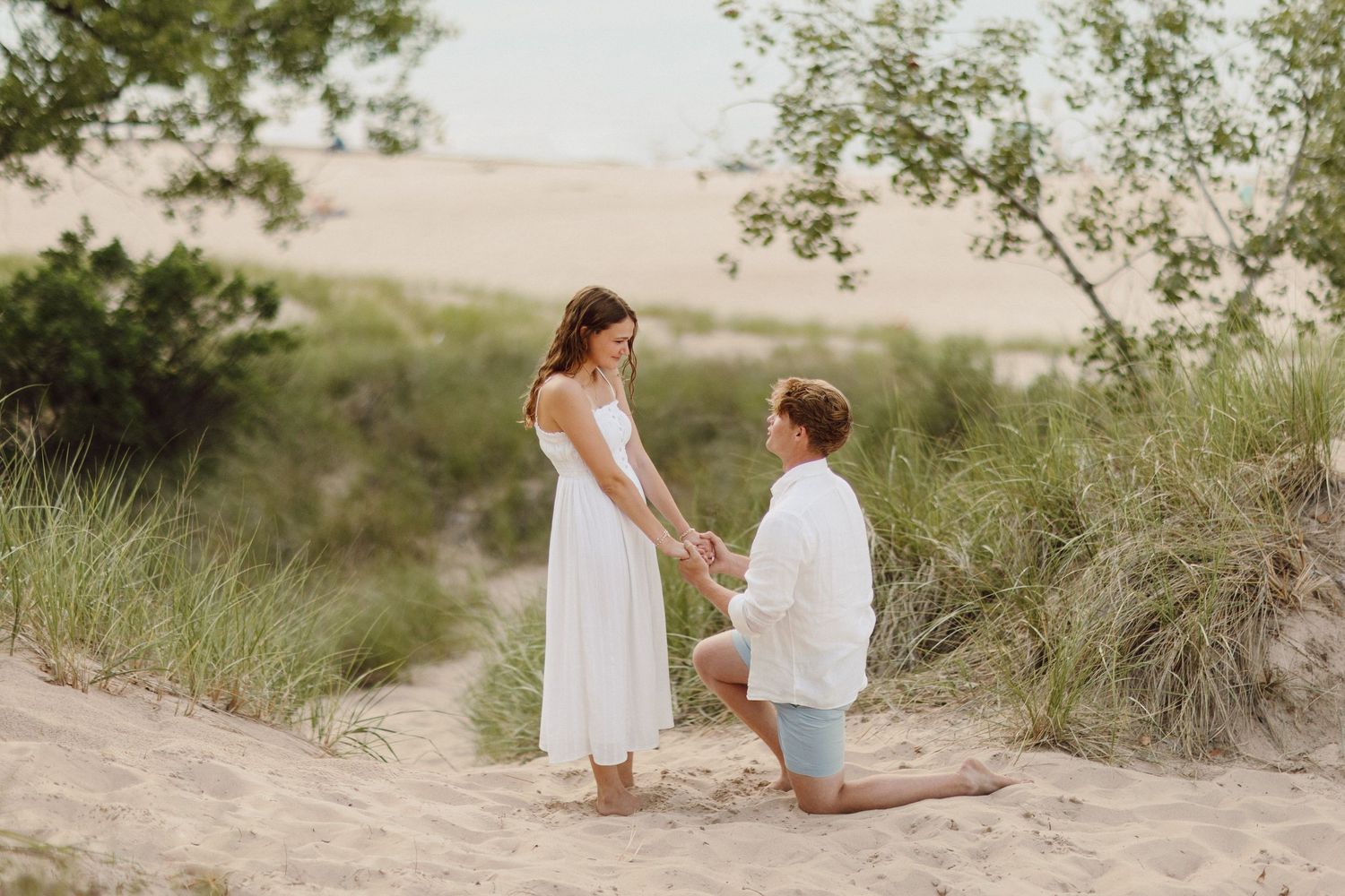 Romantic couple poses together on sandy beach dunes at sunset.