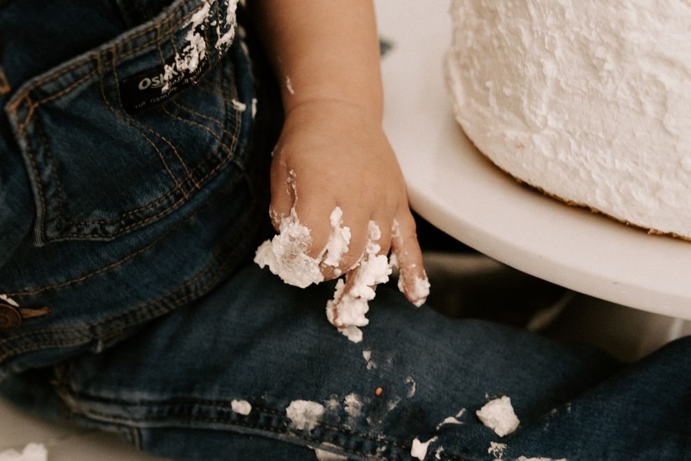 White frosting smeared on dark denim jeans next to a cake or dessert plate.
