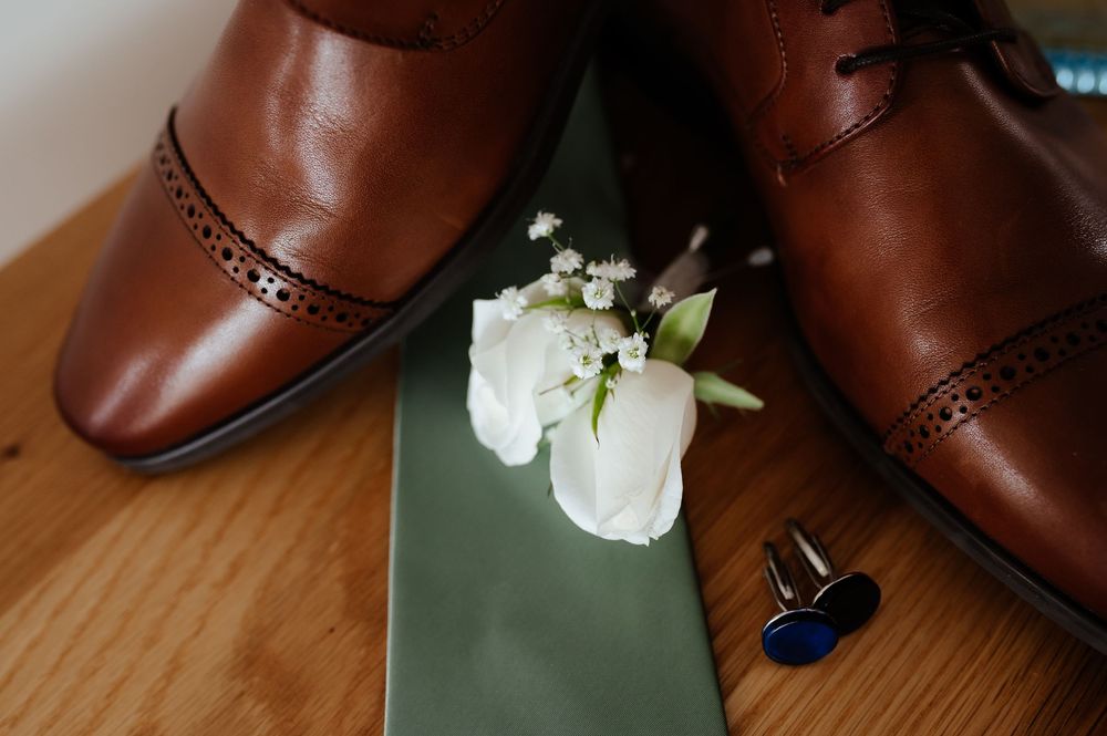 A close-up view of brown leather dress shoes with white floral decorations displayed on a wooden surface.