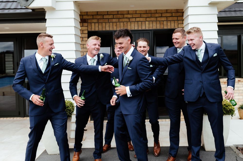 Groomsmen in navy suits sharing a candid laughing moment outside a brick building.