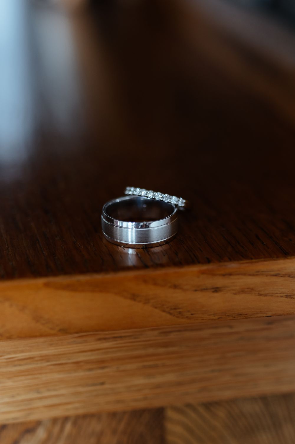 Wedding rings sit on a wooden surface in a minimalist composition showing their metallic details and diamond accents.