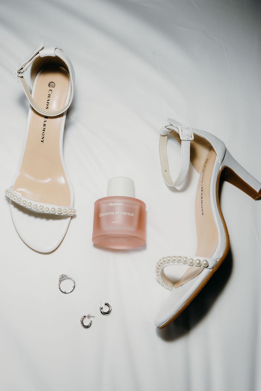 Wedding accessories including white heels, rings, and perfume arranged on light gray background.