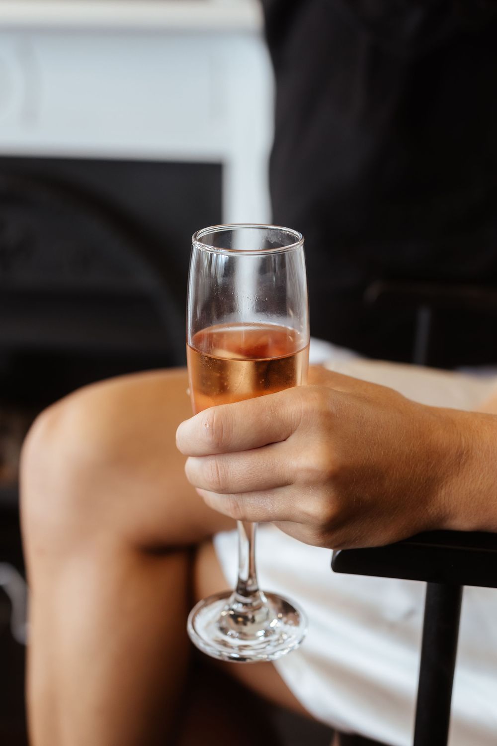 Hands holding wine glasses with rose-colored wine in a toast against a dark background.