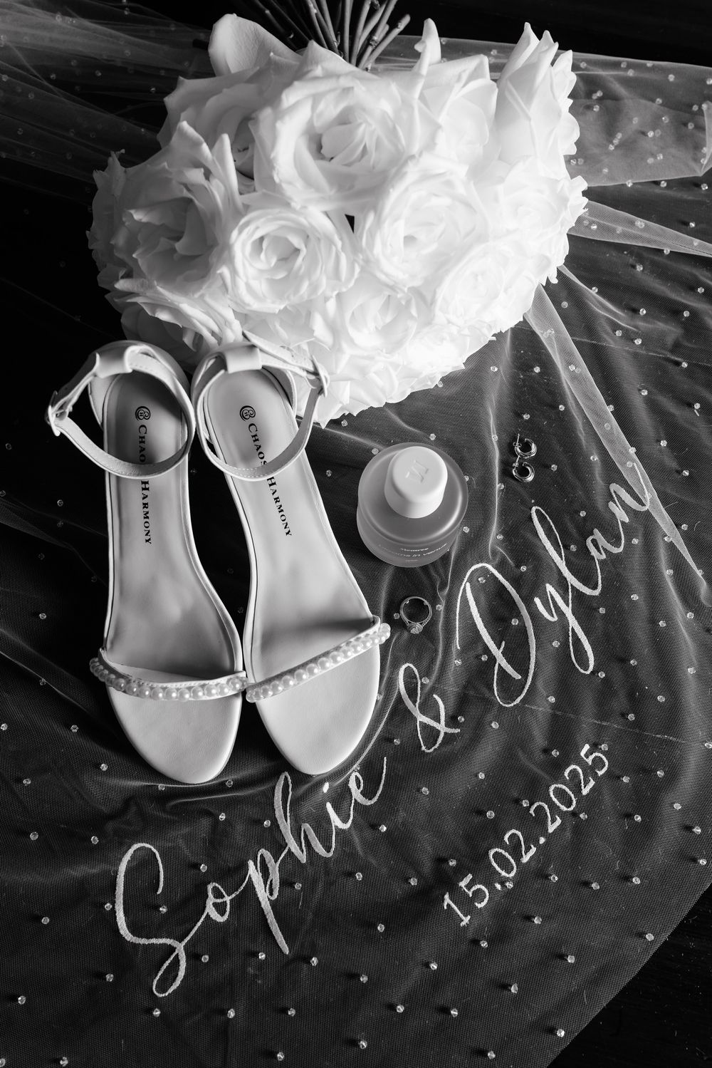 White bridal shoes with floral details and date inscription displayed on dark fabric.