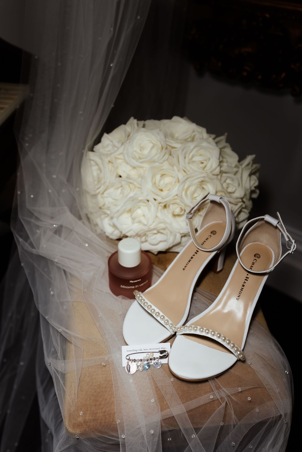 White wedding roses and delicate bridal shoes arranged on flowing tulle veil.