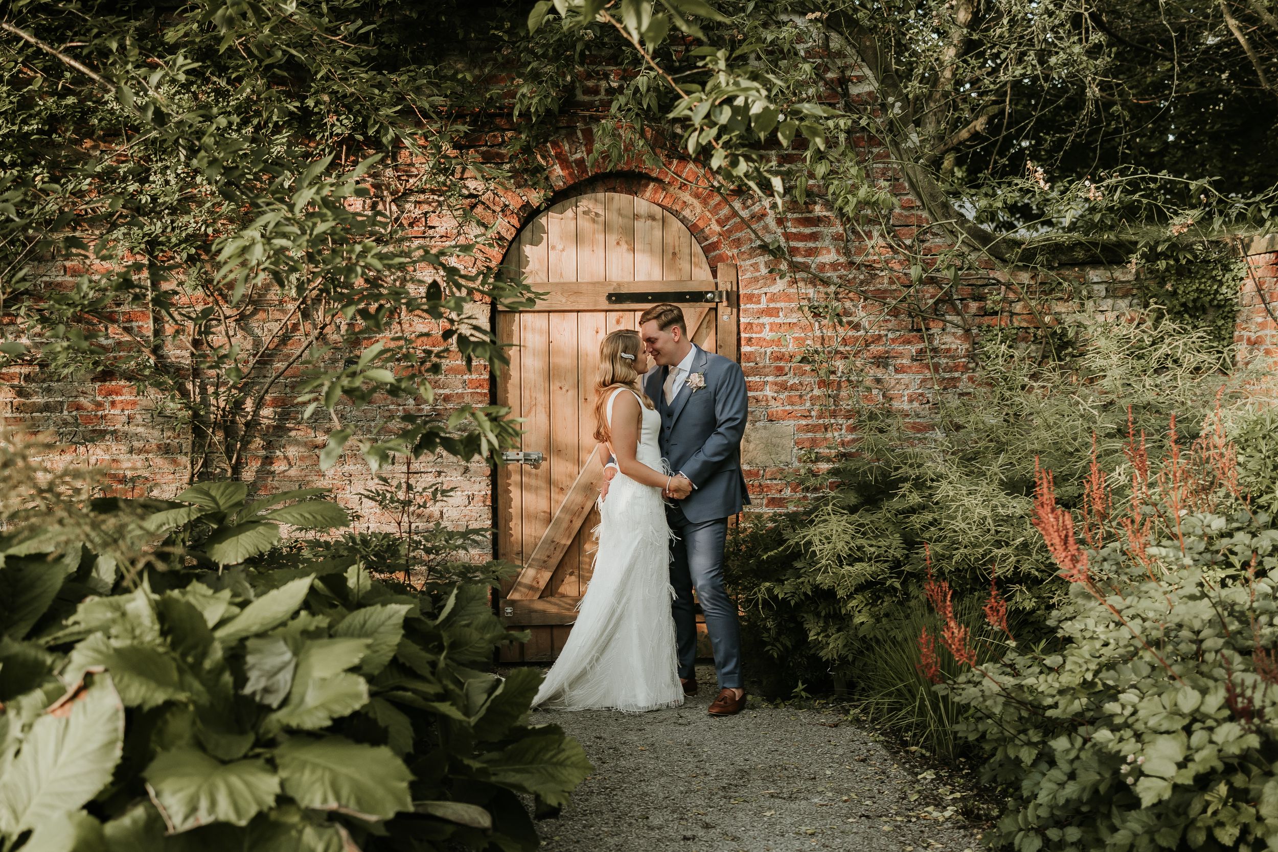 A couple shares a romantic moment in the lush garden fig house gardens at Middleton lodge with brick walls and greenery surrounding them.