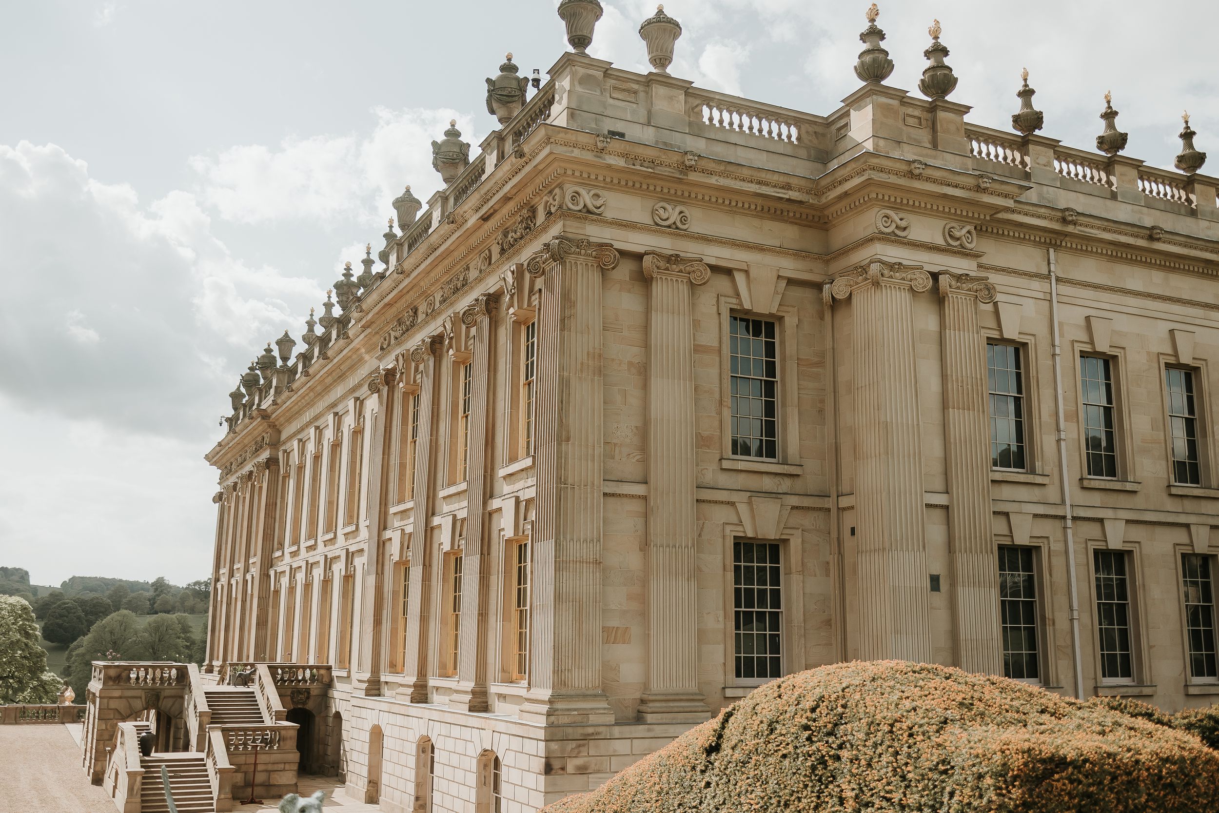 Ornate architectural details of Chatsworth house with stone columns and decorative finials against cloudy sky.