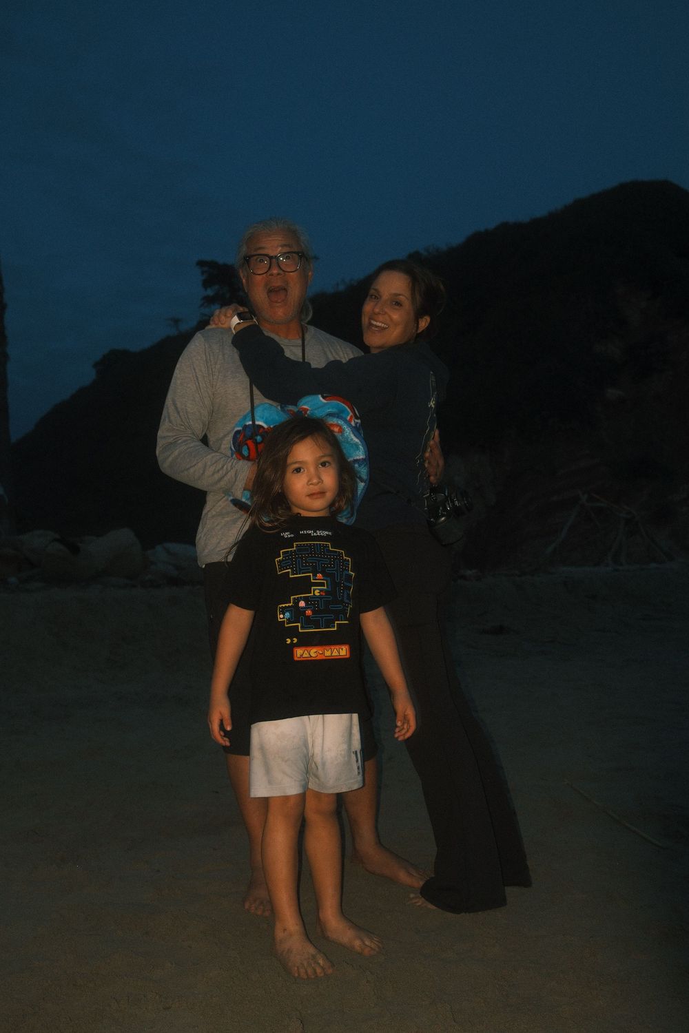 A group of people gather on a dark beach at dusk wearing casual clothing.