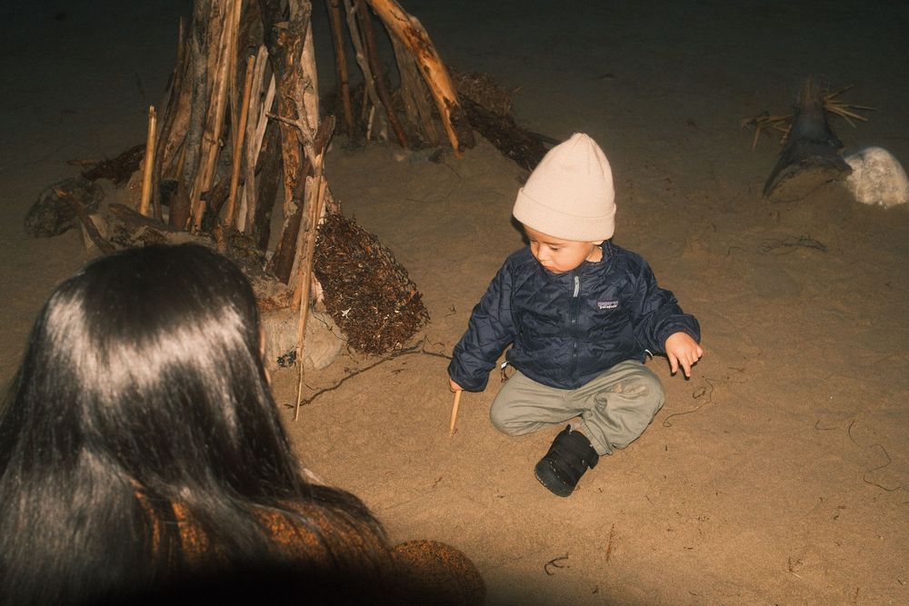 People sitting around a campfire at night in a dark outdoor setting.