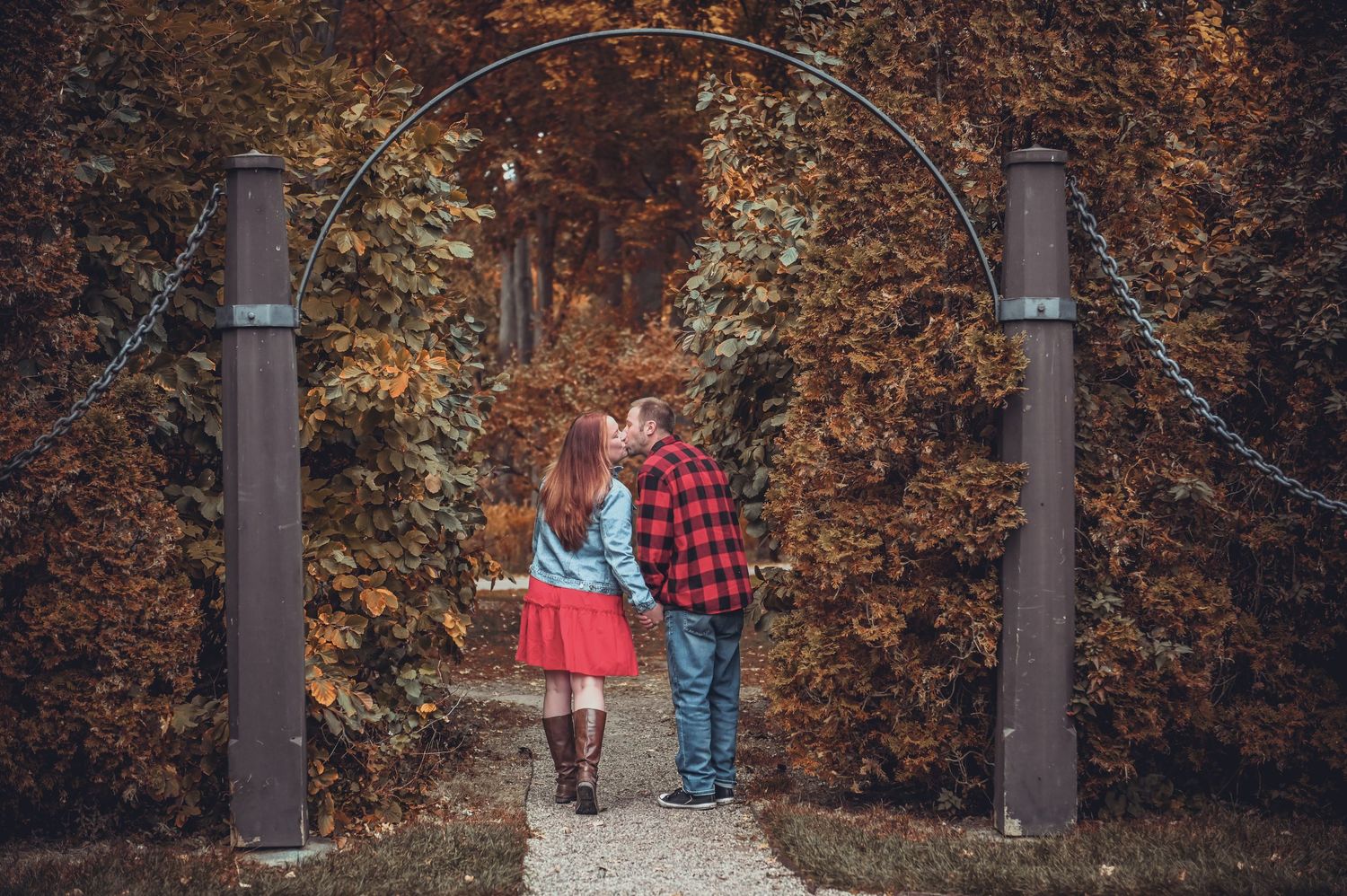 A romantic autumn scene with a couple kissing under a rustic garden arch surrounded by fall foliage.
