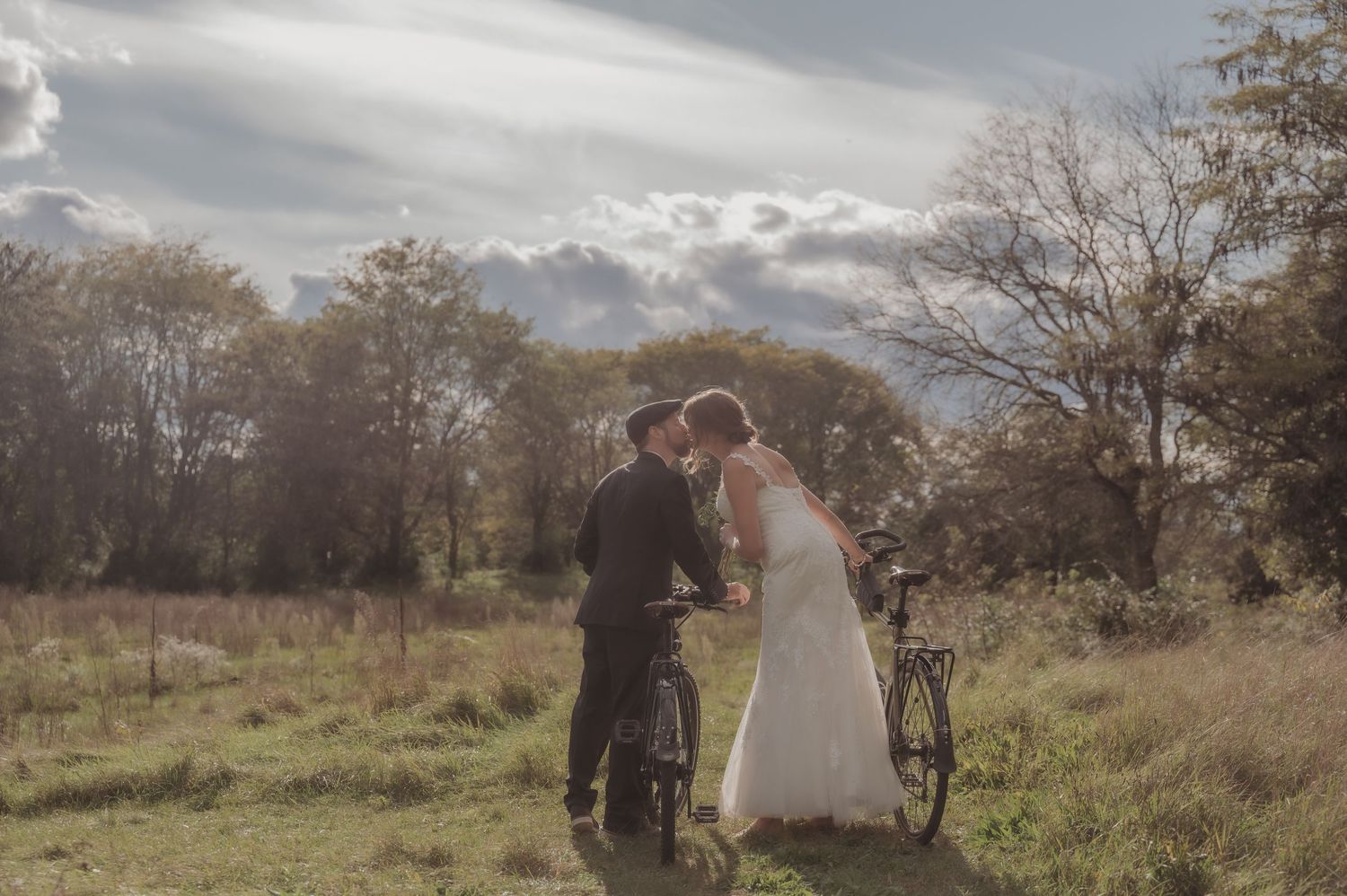 A couple poses together in a rustic outdoor setting with autumn trees and golden light in the background.