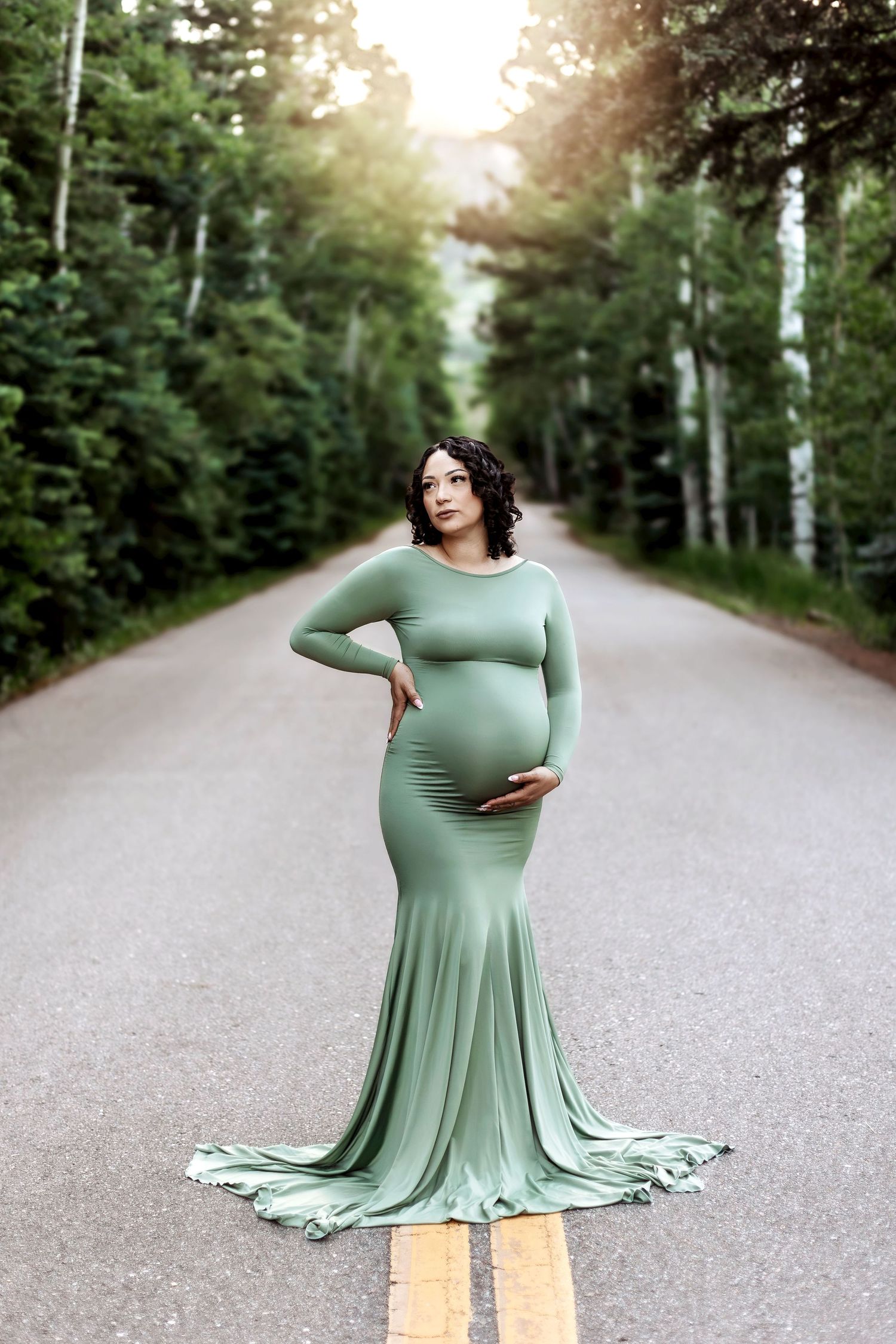 Dreamy maternity photoshoot featuring soft pink flowing dress against moody cloudy backdrop with dramatic lighting.