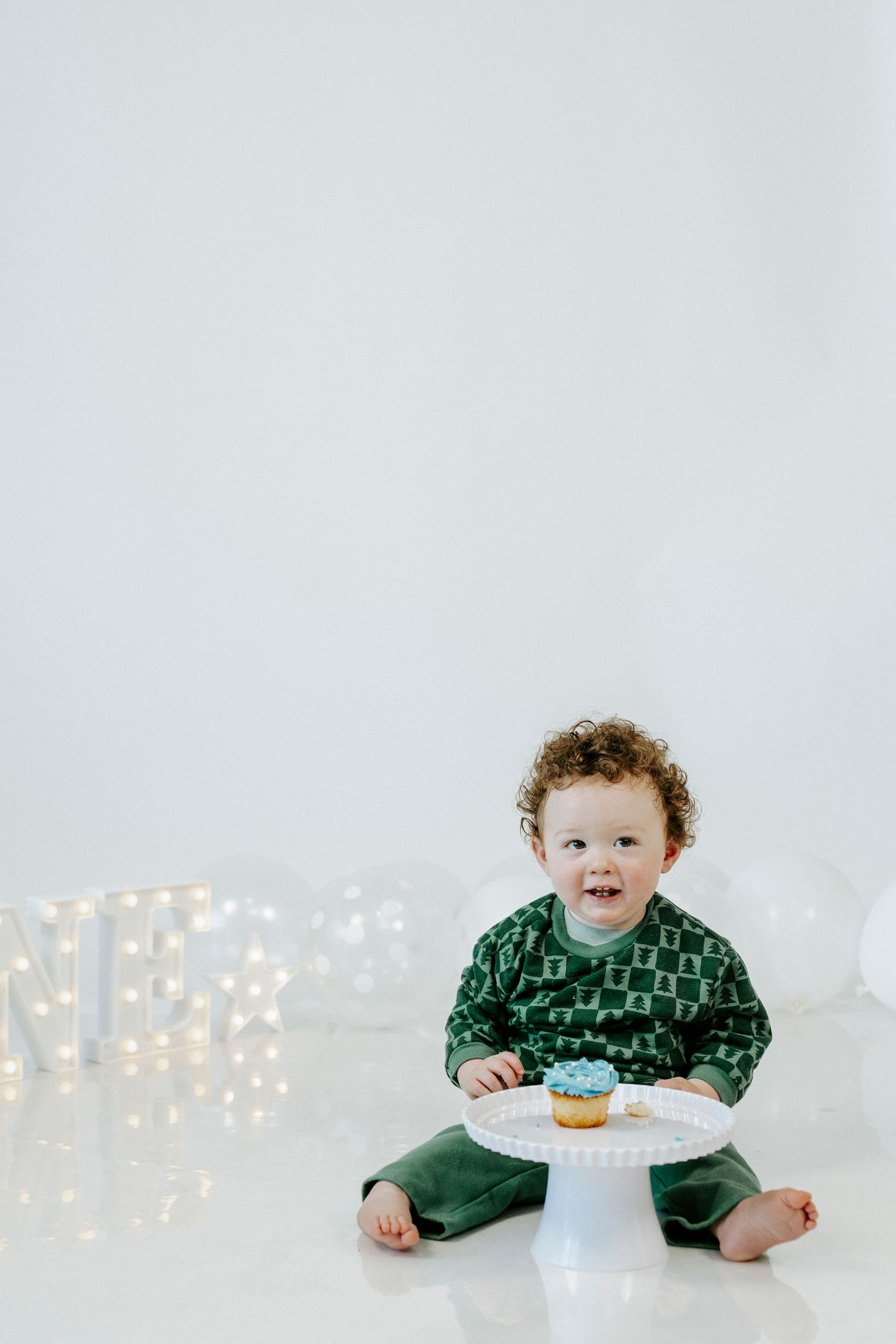 A series of four photos showing a toddler in a green sweater sitting with a birthday cake against a white background.