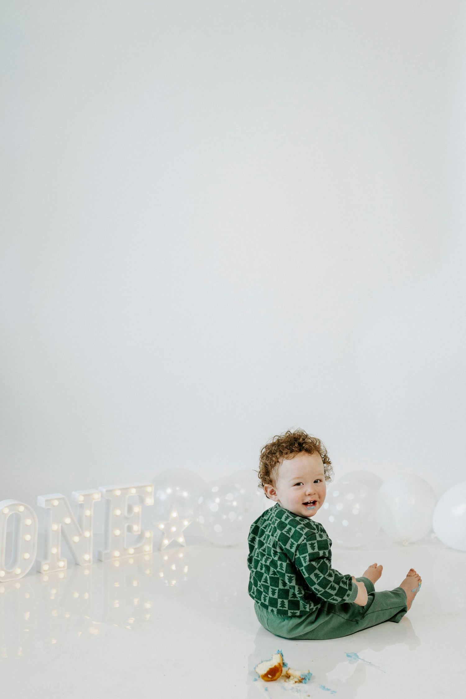 Small child in green sweater sits on floor near illuminated letters against white background.