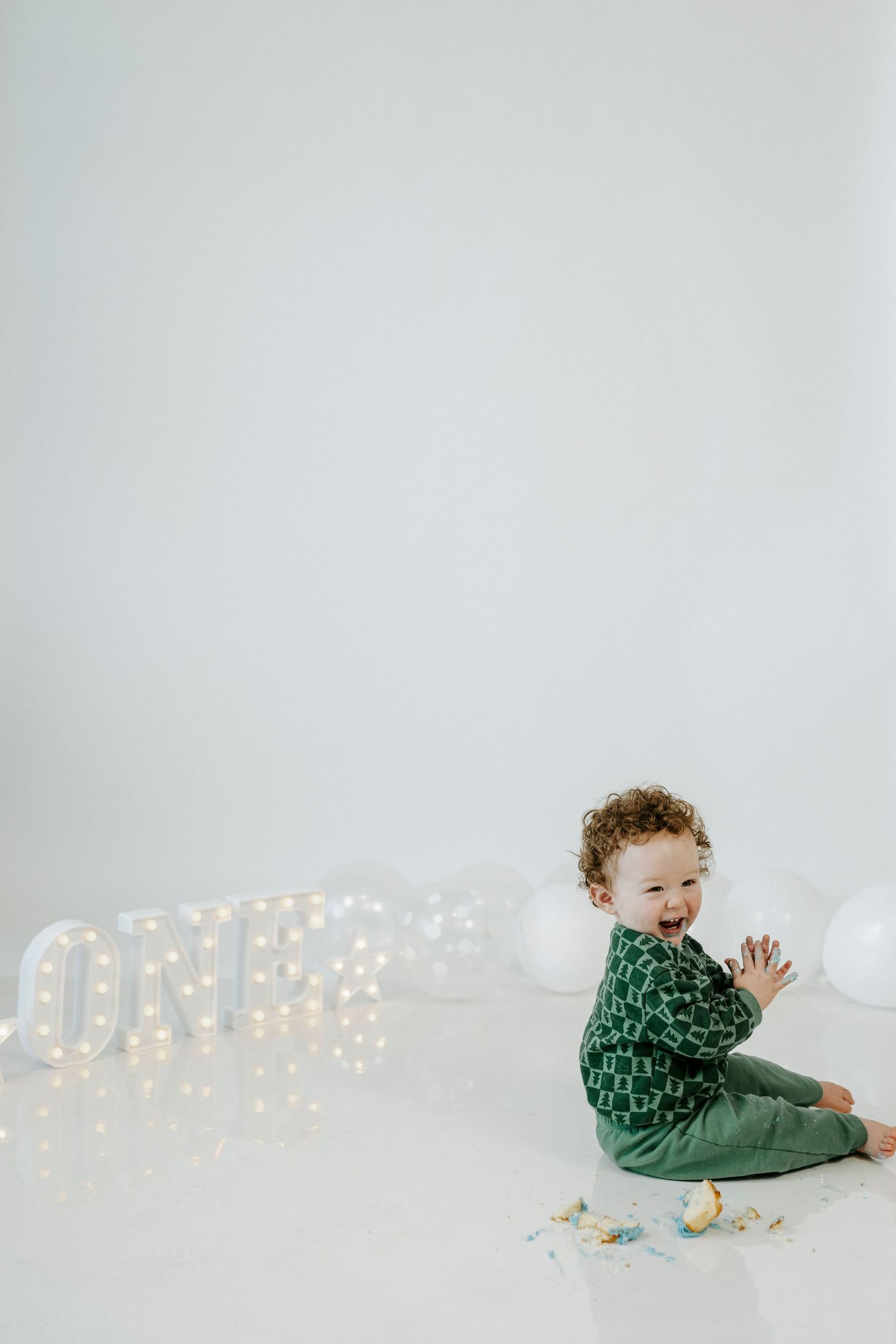 A small child in green clothing sits and claps while illuminated letters spell 'ONE' in the background.