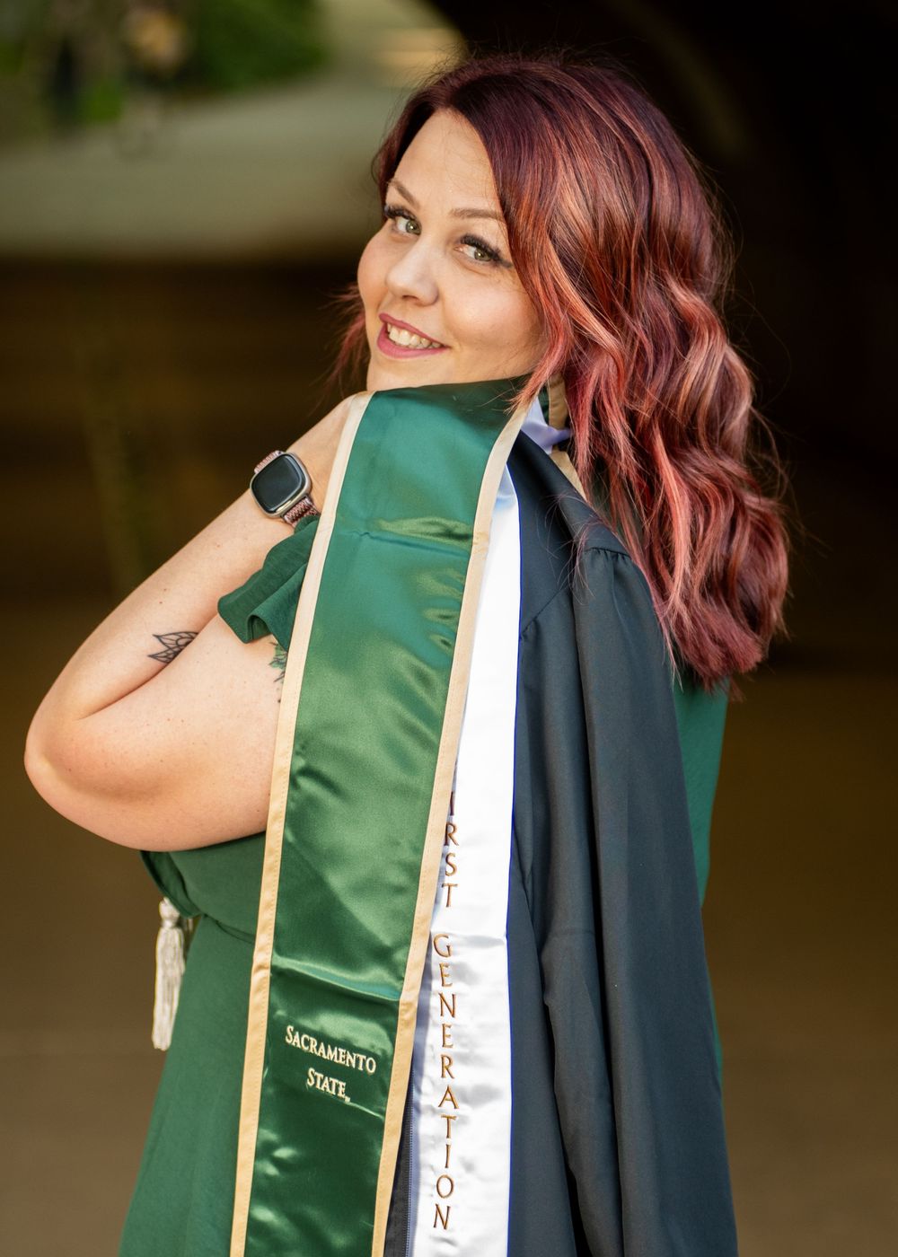 Woman with burgundy hair wearing a graduation gown holds and adjusts her green academic stole in multiple poses.