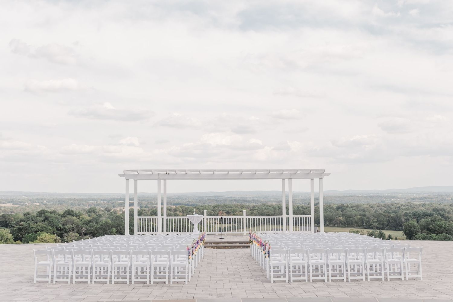 Elegant white wedding ceremony setup with pergola overlooking scenic mountain landscape.