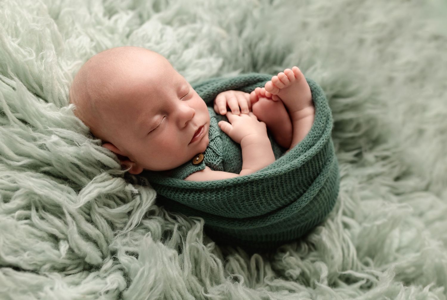 Baby boys sleeps, wrapped in soft green knits on a wool rug, captured by Charlottesville newborn, maternity, and family photographer.