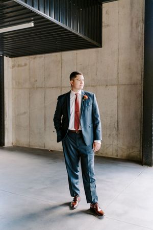 Creative sequence of groom's suit and shoes against industrial concrete wall.