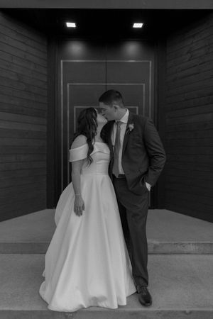 A black and white wedding photo showing a couple sharing an intimate moment in front of a modern doorway.