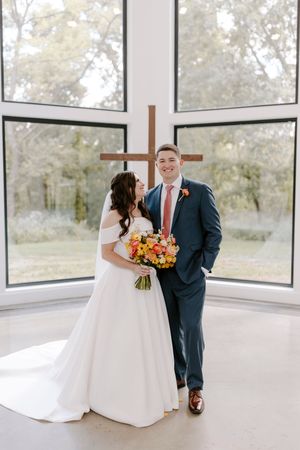 A couple shares intimate moments in a modern chapel with floor-to-ceiling windows and wooden cross details.