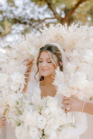 Ethereal bridal portrait surrounded by soft white flowers creating a dreamy, romantic atmosphere.