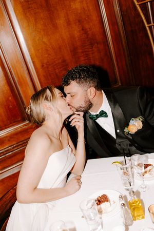 A couple shares an intimate moment at their wedding reception table with drinks and decor visible.
