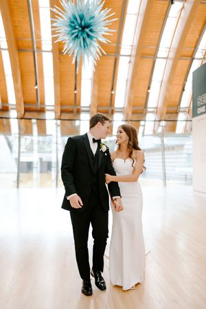 A couple in wedding attire dances in a bright wooden-floored venue with blue paper decorations hanging from above.