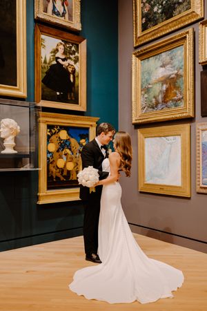 Couple in formal wedding attire share intimate moments while viewing artwork in an elegant museum gallery.