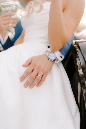 Close-up view of hands wearing wedding rings against a white dress and dark suit background.