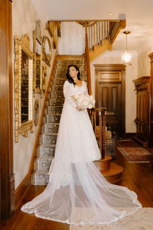 Elegant white wedding dress with long flowing train displayed on wooden staircase in traditional home interior.