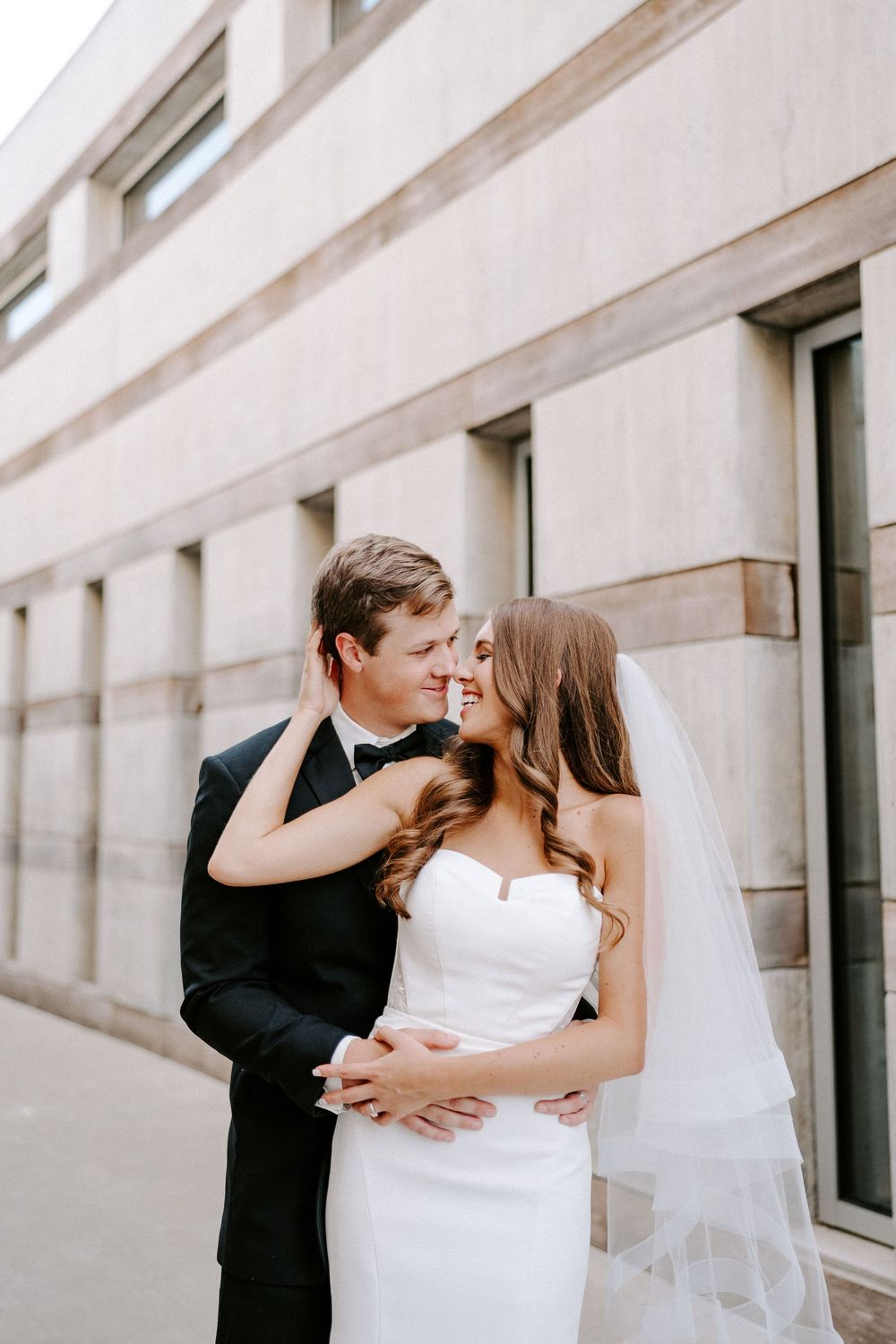 A romantic sequence of wedding photos showing a couple embracing and kissing against a modern architectural backdrop.