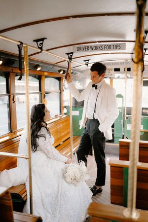 A couple in wedding attire share a romantic moment inside a vintage trolley car with wooden benches.
