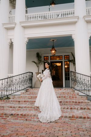 A flowing white wedding dress twirls across a brick patio with classic white columns in the background.