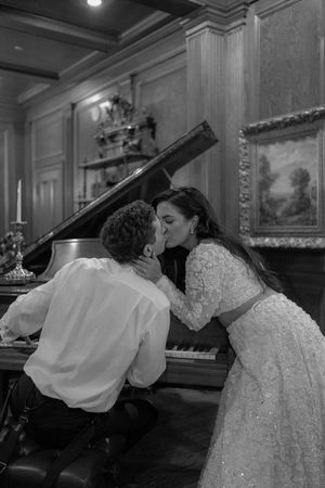 Romantic black and white photo of a couple sharing an intimate moment at a grand piano in an elegant room.