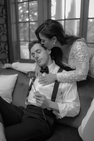 A romantic black and white portrait of a couple in formal attire embracing on a couch.